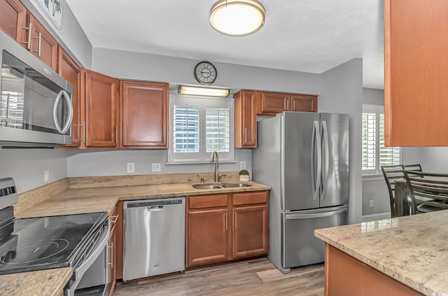 kitchen with appliances with stainless steel finishes, brown cabinets, a sink, and light wood finished floors