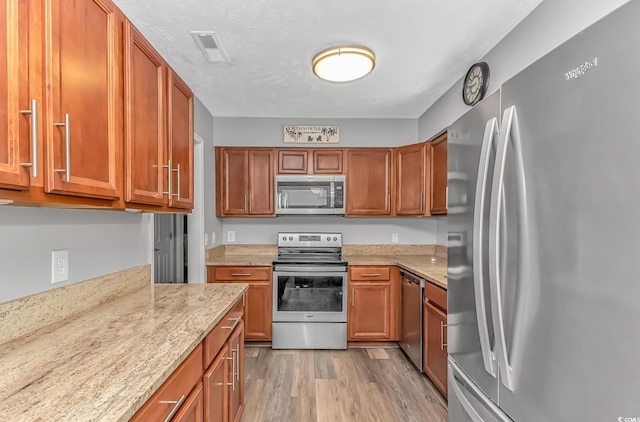 kitchen featuring stainless steel appliances, brown cabinetry, visible vents, and light wood-style floors