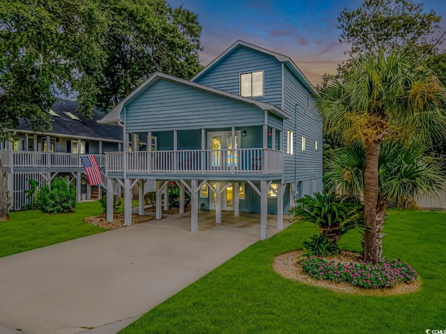 beach home with a carport, a front yard, concrete driveway, and a porch