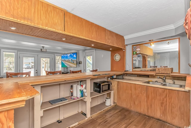 kitchen with french doors, stainless steel microwave, ornamental molding, a sink, and wood finished floors