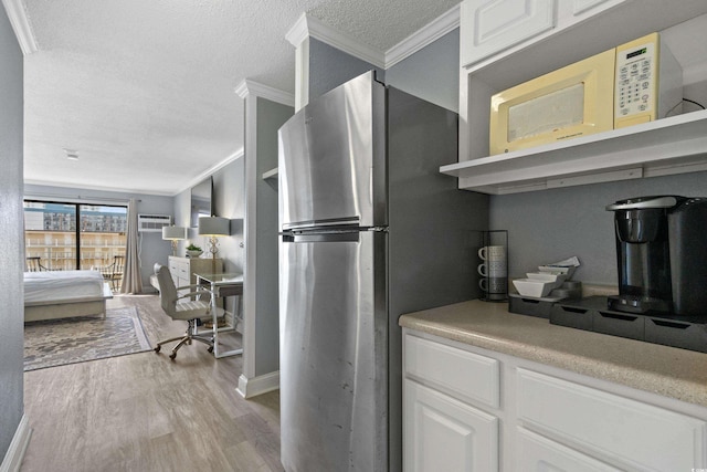 kitchen featuring light wood finished floors, white microwave, ornamental molding, freestanding refrigerator, and a textured ceiling