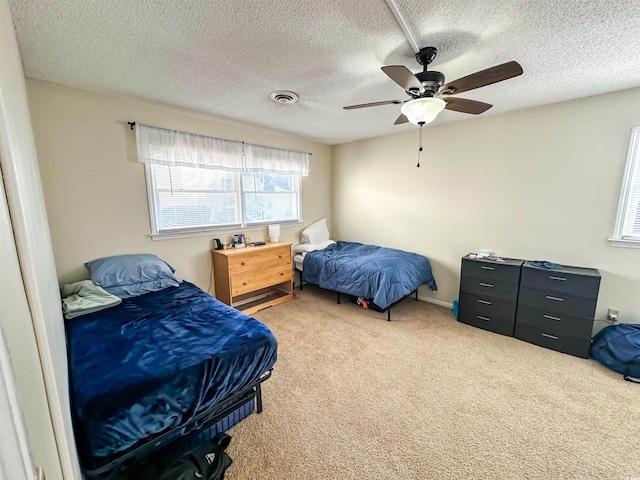 bedroom featuring visible vents, light colored carpet, a textured ceiling, and ceiling fan