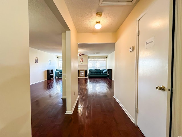 hall featuring dark wood-style floors, a textured ceiling, and baseboards