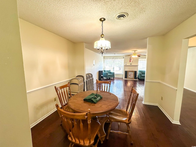 dining space featuring hardwood / wood-style floors, visible vents, baseboards, a fireplace, and ceiling fan with notable chandelier