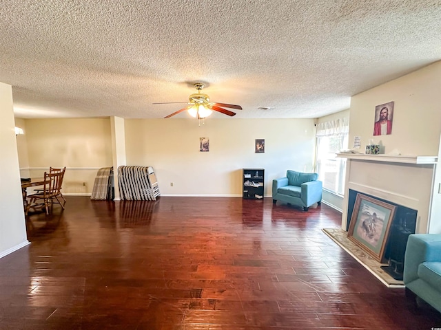 living area with a glass covered fireplace, wood finished floors, baseboards, and a ceiling fan