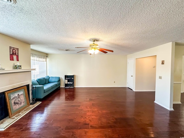 unfurnished living room with wood finished floors, baseboards, a fireplace with raised hearth, ceiling fan, and a textured ceiling