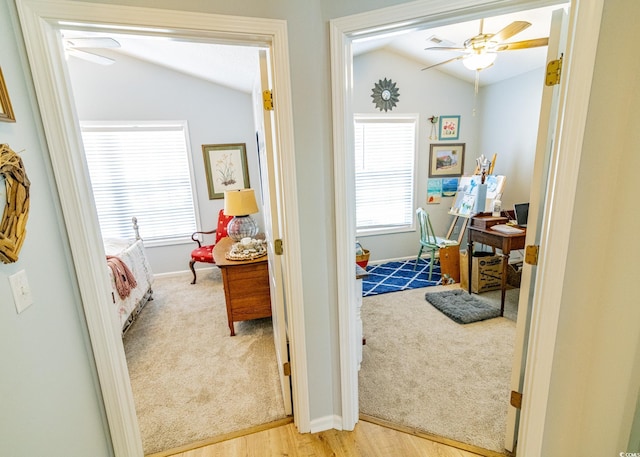 hallway with lofted ceiling, a healthy amount of sunlight, light carpet, and light wood finished floors