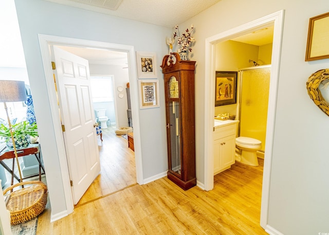 corridor featuring light wood-style floors, a textured ceiling, and baseboards