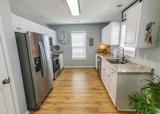 kitchen with light wood-style flooring, appliances with stainless steel finishes, white cabinets, a sink, and a textured ceiling