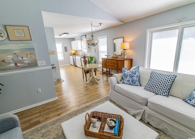 living room with light wood-type flooring, baseboards, and vaulted ceiling