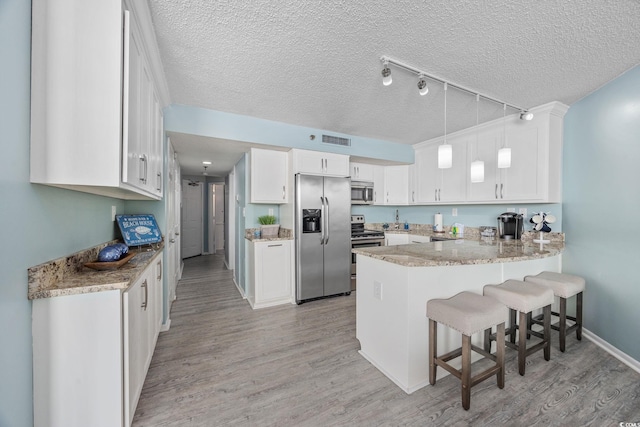 kitchen with a peninsula, white cabinetry, light wood-type flooring, and appliances with stainless steel finishes