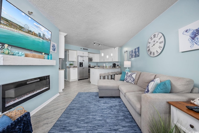 living area with baseboards, a glass covered fireplace, a textured ceiling, light wood-style floors, and track lighting