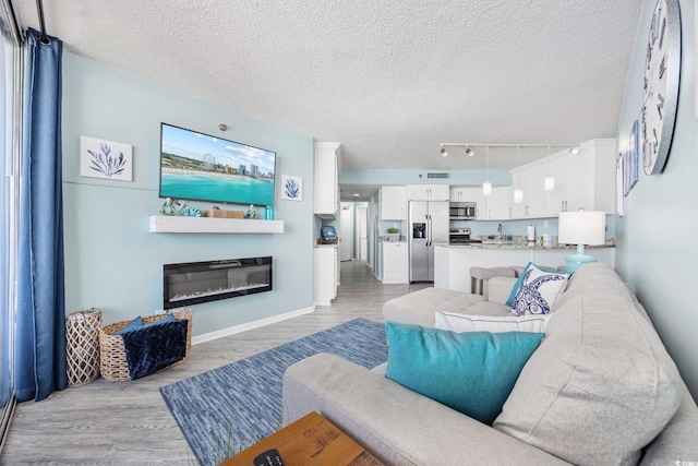 living room with light wood-style flooring, baseboards, a textured ceiling, and a glass covered fireplace