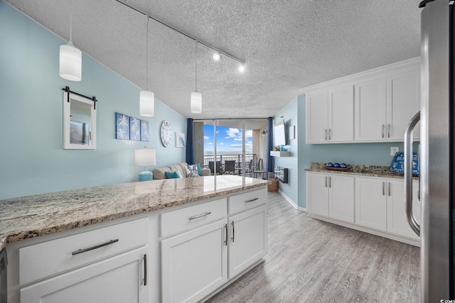 kitchen with a textured ceiling, white cabinetry, freestanding refrigerator, light wood finished floors, and pendant lighting