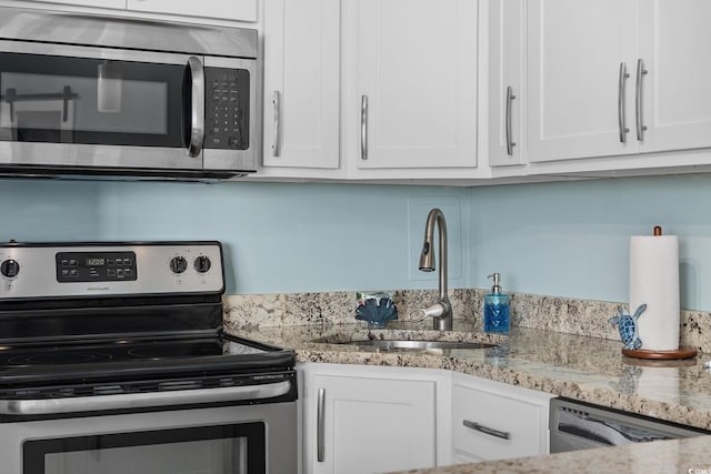 kitchen featuring light stone counters, appliances with stainless steel finishes, white cabinets, and a sink