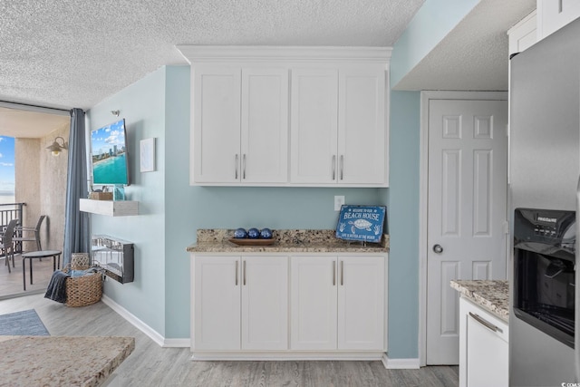 kitchen featuring light wood-style floors, stainless steel fridge, light stone counters, and white cabinets