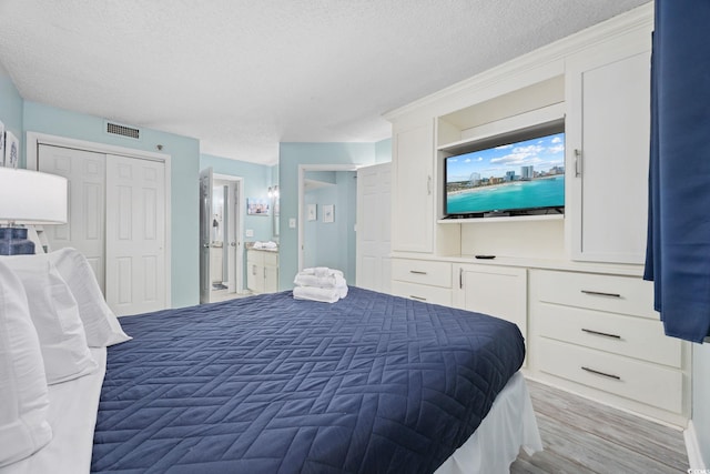 bedroom featuring connected bathroom, visible vents, a textured ceiling, and wood finished floors