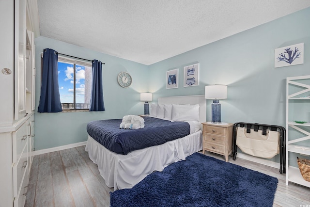 bedroom with a textured ceiling, baseboards, and wood finished floors