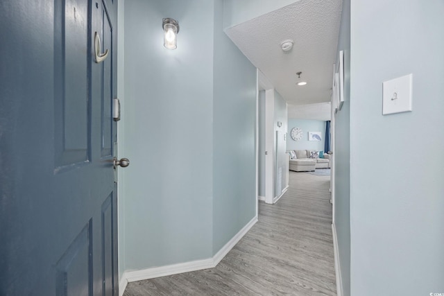 hallway featuring a textured ceiling, baseboards, and wood finished floors