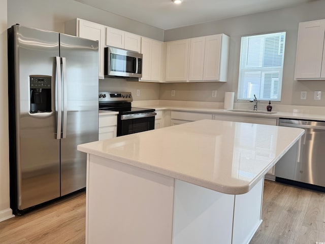 kitchen featuring a kitchen island, stainless steel appliances, light wood-style floors, white cabinetry, and a sink