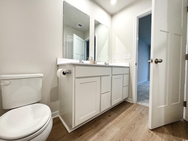 bathroom featuring visible vents, toilet, vanity, wood finished floors, and baseboards