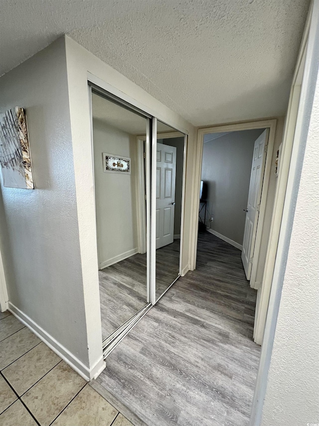 hallway with baseboards, a textured ceiling, and wood finished floors