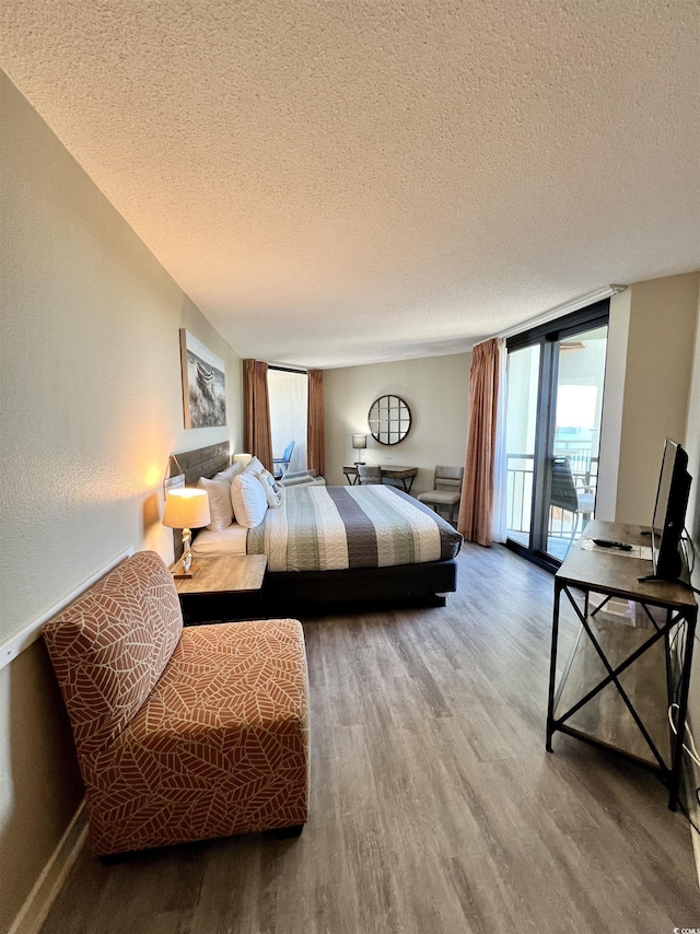 bedroom with a textured ceiling, wood finished floors, floor to ceiling windows, and access to outside