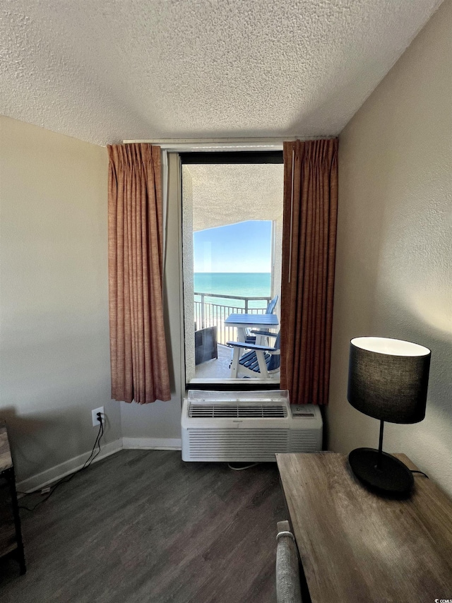 interior space featuring baseboards, a water view, a textured ceiling, a wall mounted AC, and dark wood-style flooring