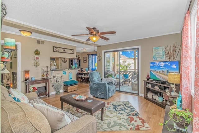 living room with a textured ceiling, visible vents, wood finished floors, and ornamental molding