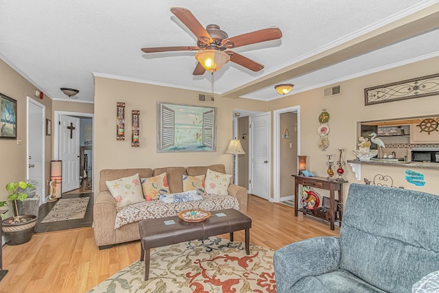 living room with ornamental molding, a ceiling fan, visible vents, and wood finished floors