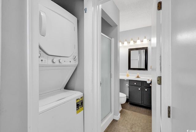 full bath with a textured ceiling, toilet, vanity, stacked washer / drying machine, and a stall shower