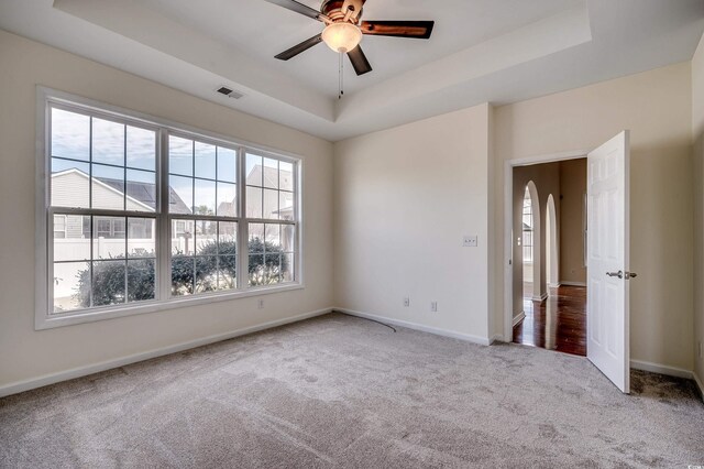 empty room featuring arched walkways, carpet flooring, a raised ceiling, and visible vents