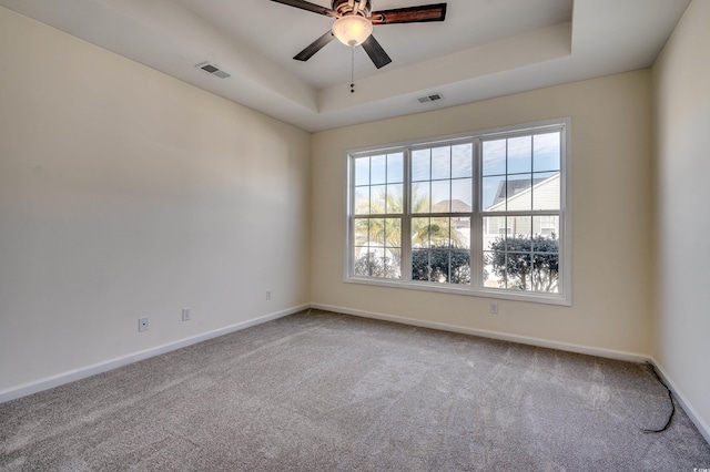 carpeted empty room featuring a ceiling fan, a raised ceiling, visible vents, and baseboards