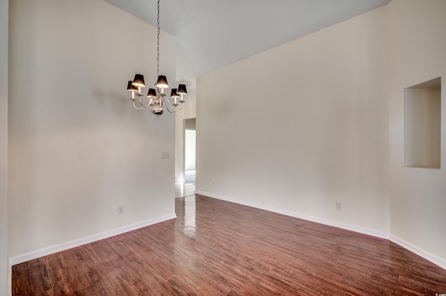 unfurnished room with vaulted ceiling, dark wood-style flooring, a notable chandelier, and baseboards