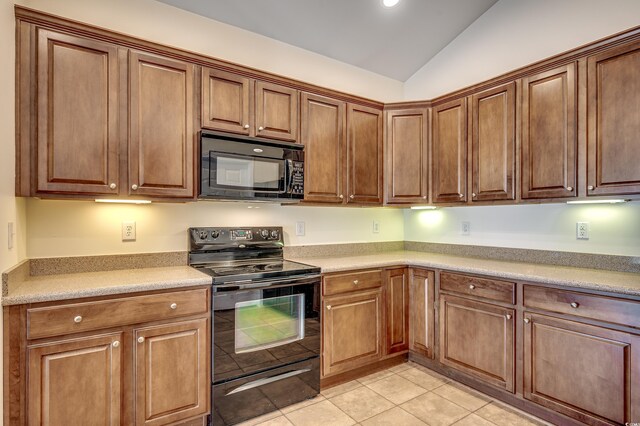 kitchen featuring lofted ceiling, light tile patterned floors, light countertops, black appliances, and brown cabinetry