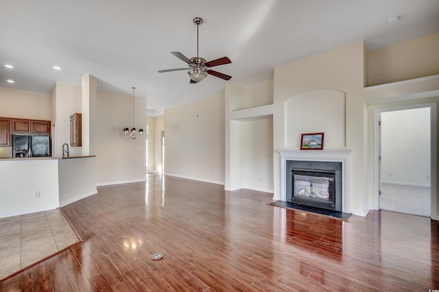 unfurnished living room with a glass covered fireplace, a sink, wood finished floors, high vaulted ceiling, and ceiling fan with notable chandelier