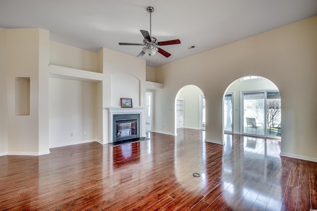 unfurnished living room with ceiling fan, baseboards, wood finished floors, and a glass covered fireplace