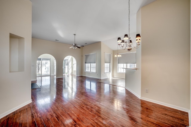 empty room with arched walkways, ceiling fan with notable chandelier, a high ceiling, wood finished floors, and baseboards