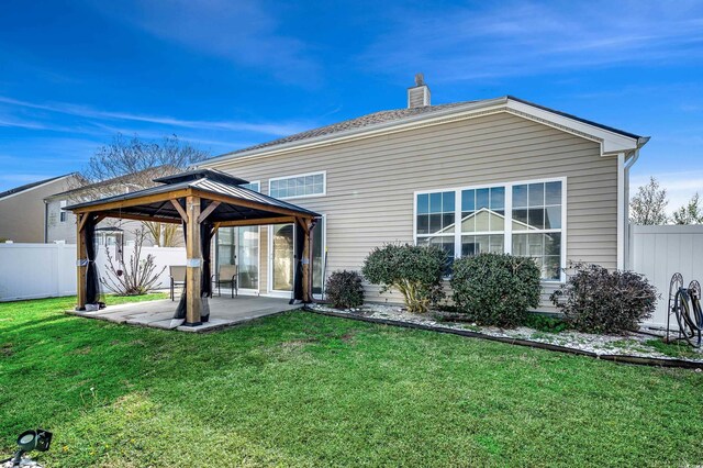 rear view of house with a lawn, a patio, a chimney, fence private yard, and a gazebo