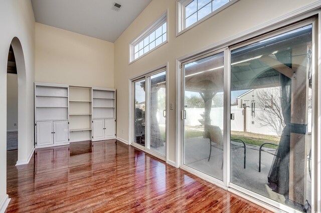 doorway with baseboards, visible vents, dark wood finished floors, arched walkways, and a high ceiling