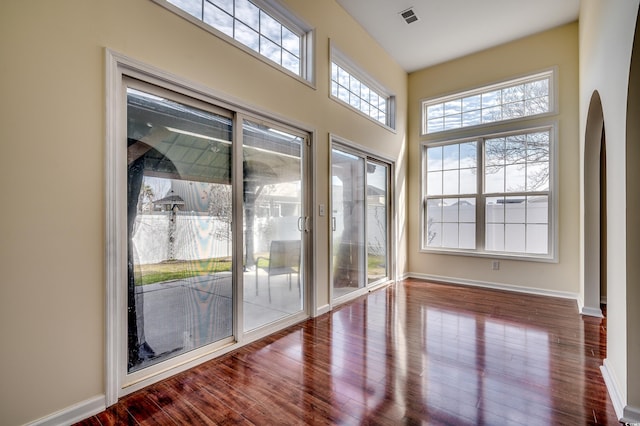 interior space featuring baseboards, visible vents, dark wood finished floors, and arched walkways