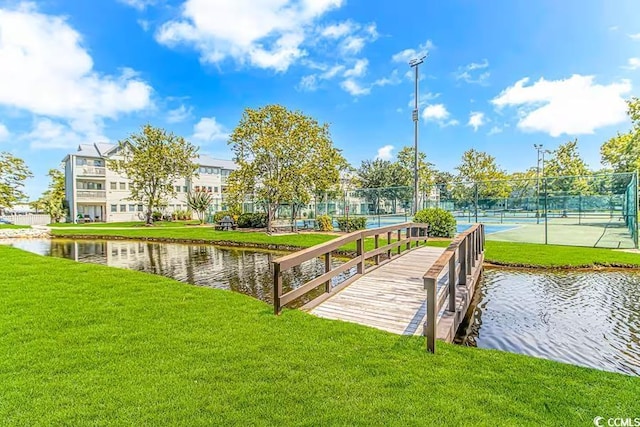 dock area featuring a water view, a lawn, and fence