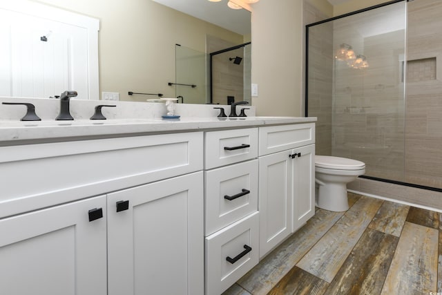 bathroom featuring wood finished floors, double vanity, a sink, a shower stall, and toilet