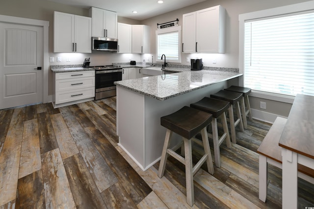 kitchen with light stone countertops, a kitchen bar, appliances with stainless steel finishes, a peninsula, and white cabinets