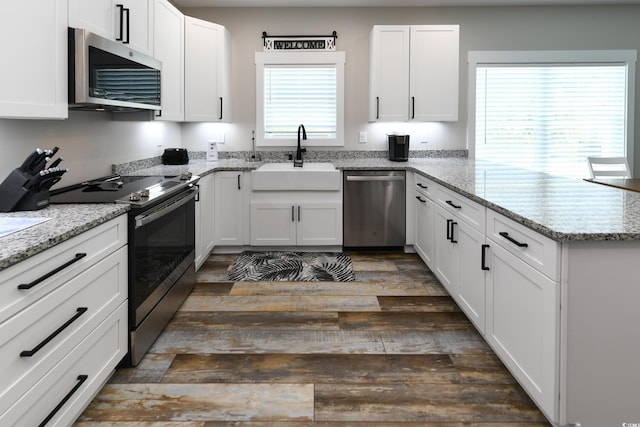 kitchen with a sink, dark wood finished floors, appliances with stainless steel finishes, a peninsula, and white cabinets