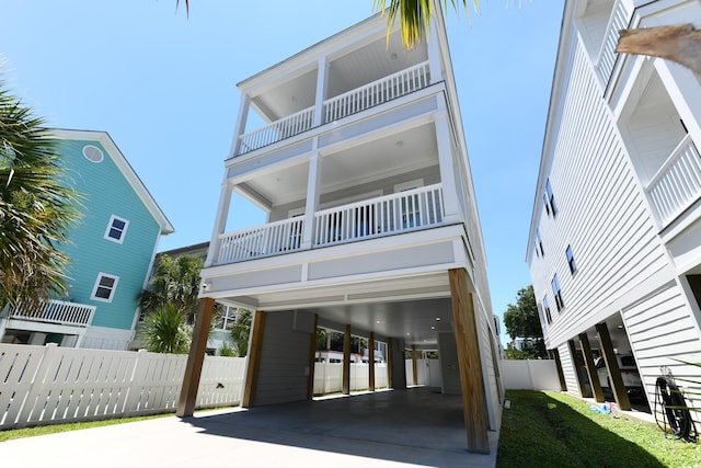 raised beach house featuring a carport, a balcony, concrete driveway, and fence