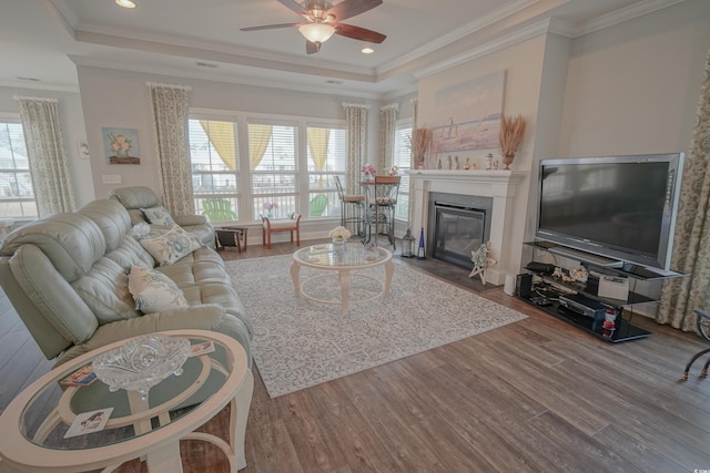 living room featuring a fireplace with flush hearth, crown molding, a raised ceiling, and wood finished floors