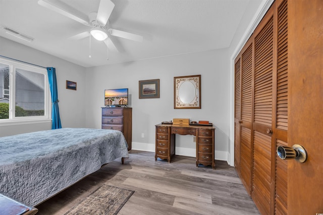 bedroom with baseboards, visible vents, ceiling fan, wood finished floors, and a closet