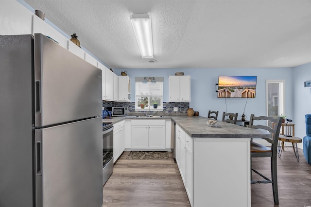 kitchen with stainless steel appliances, a breakfast bar, a peninsula, wood finished floors, and a sink