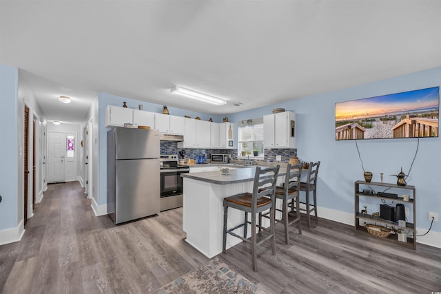 kitchen with under cabinet range hood, a peninsula, white cabinets, appliances with stainless steel finishes, and decorative backsplash